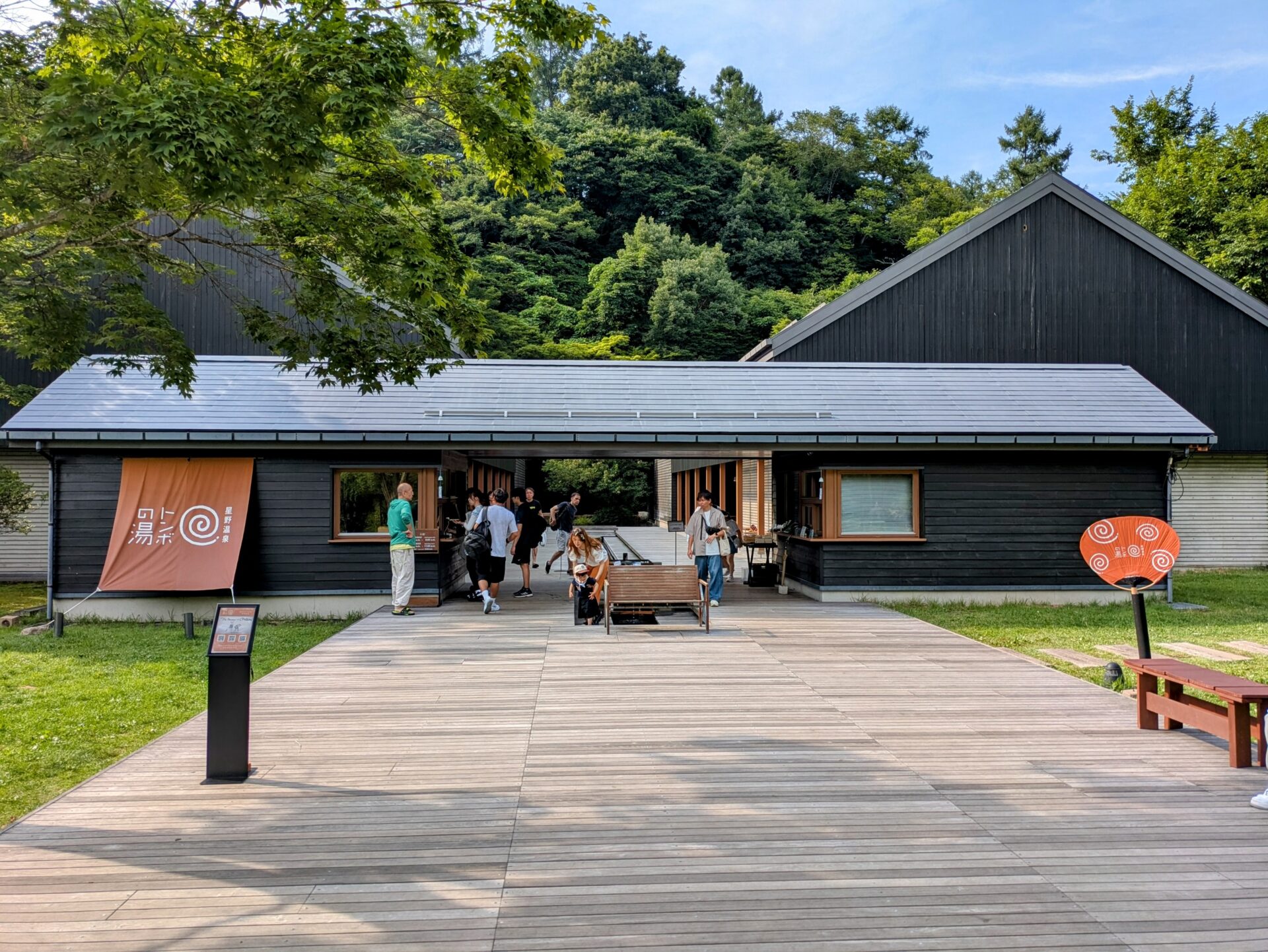 長野県軽井沢にある星野温泉トンボの湯の入り口。黒い木造建築と木製のデッキ、そして緑豊かな自然が調和したモダンな外観。