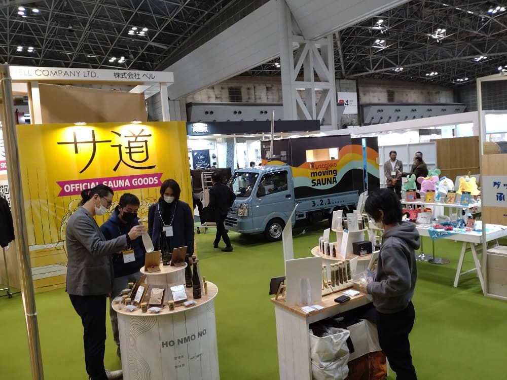 サウナフェアのイベント会場で、サウナグッズや移動式サウナの展示を見ている人々。