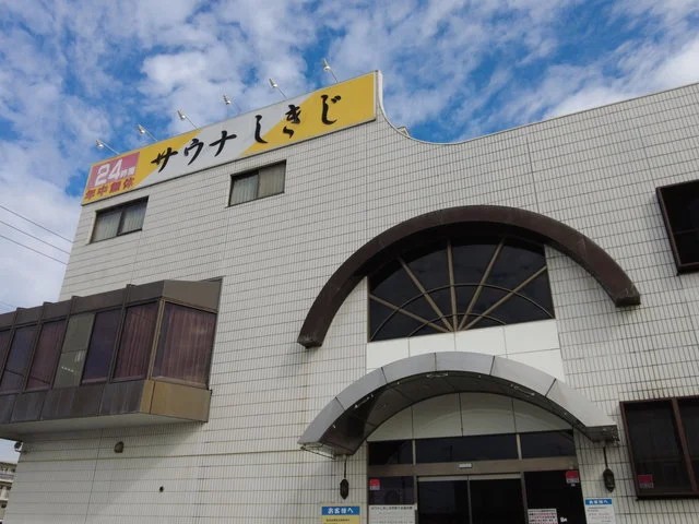 サウナの聖地「サウナしきじ」の建物の外観。黄色い看板と24時間営業の表示が目印。